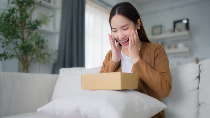 Happy young Asian woman opening delivery package at home. Beautiful female customer open box and...