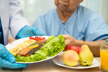 Asian elderly woman patient eating salmon stake and vegetable salad for healthy food in hospital.