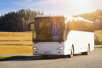 White coach bus at speed on road on a sunny autumn afternoon, blue sky and clouds.