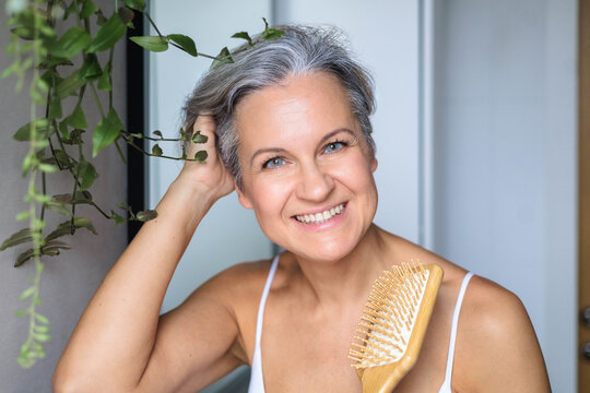 Portrait of a beautiful, smiling gray-haired European woman with a wooden comb. Concept anti-age.