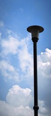 Tall lamp post against a bright blue sky with fluffy white clouds