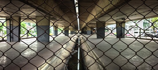 View through a chain-link fence of an urban underpass with concrete pillars