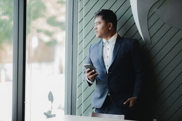A handsome, successful businessman in a modern suit uses a smartphone, surfs the internet, and texts, chats, and holds online meetings.
