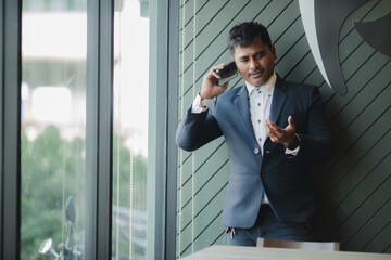 Fototapeta premium A handsome, successful businessman in a modern suit uses a smartphone, surfs the internet, and texts, chats, and holds online meetings. 