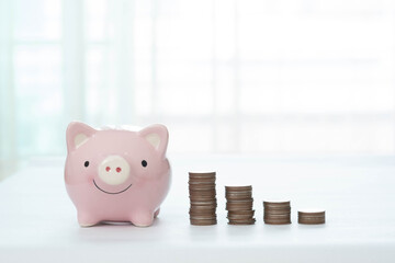 Piggy bank and stack of coins on white tabletop and blurred background. Finance and money saving concept.