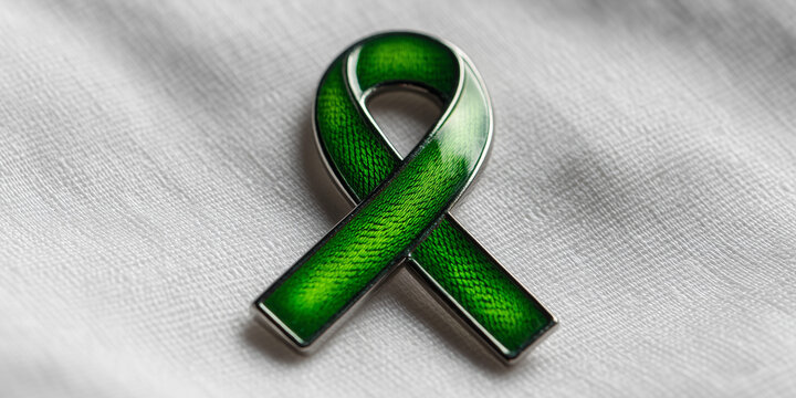 Green awareness ribbon pin on a light fabric background
