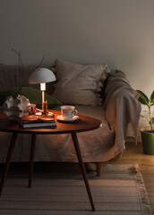 Cozy evening interior of the living room - sofa, wooden table with decor, candle, lamp, cup. Cozy house concept