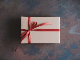 Simple Beige Gift Box Wrapped with Red Ribbon on Textured Surface