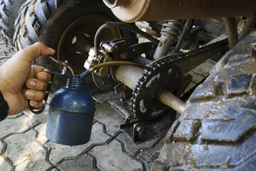 Close up of focused mechanic hand lubricating an ATV chain with blue oil can. This vehicle maintenance shows preparation for an off road race or repair service © CoreRock