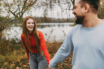 Fototapeta premium happy pair holding hands during energetic autumn walk amid colorful trees and fallen leaves