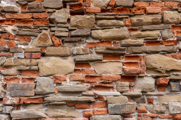 Old brick and stone wall texture with irregular pattern. Weathered masonry surface showing red bricks and natural sandstone blocks in rustic construction style.