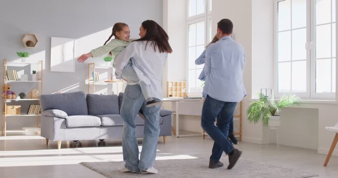 Slow motion of happy family of four having fun dancing with children in the living room at home. Young parents father, mother spending time together kids. Family time and leisure concept. 4k video.