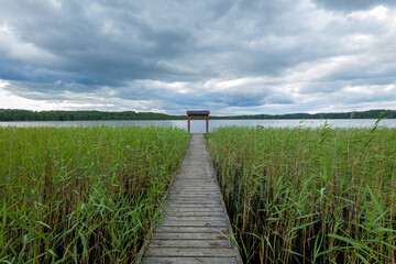 A view of the lake. A wooden pier nestled among the reeds with a small wooden bower. Lake Choczewskie, Choczewo, Kashubia, Poland