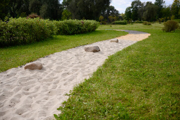 Sandy barefoot trail through park, gently meandering between green lawns. Barefoot trail in park with variety of textures. Reflexology, relaxation, and relaxing walking route.
