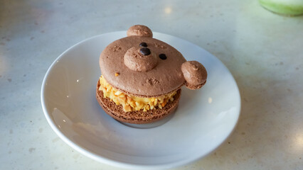 Cute bear-shaped macaron dessert on a white plate, featuring chocolate and caramel flavors, showcasing delightful pastry artistry and creativity