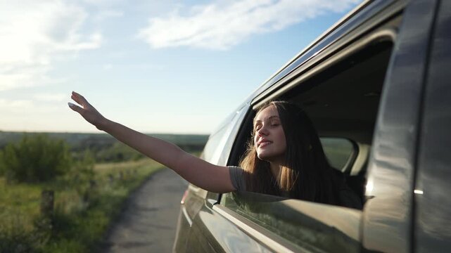 Woman enjoys road trip in car. Smiling woman leans out car window during scenic road adventure. Joyful trip captures essence carefree road journey. Woman embraces freedom and excitement on car trip.