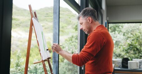 Fototapeta premium Mature, man and painting canvas with easel for art, drawing or creative sketching in home. Male person, artistic or landscape painter with brush, frame or artwork for craft, skill or talent in house