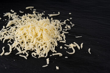 Grated mozzarella cheese on black background. Shredded mozarella texture