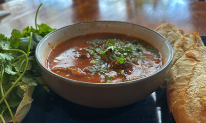 A hearty bowl of Vietnamese beef stew, Bo Kho, served with a fresh baguette and herbs