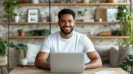 Young man smiling at laptop in cozy home office with plants and shelves