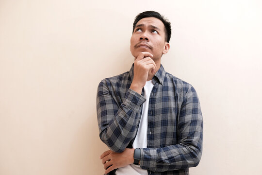 Southeast Asian man wearing flannel shirt thinking about something while looking to upper right corner, on white isolated background - Powered by Adobe