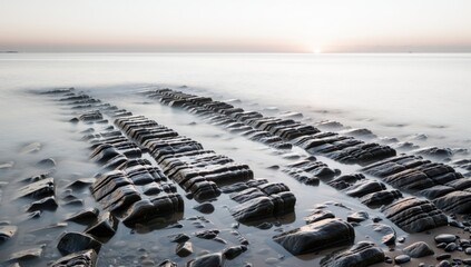 Long exposure shot of rock formations in the sea at sunset, creating a serene and peaceful scene