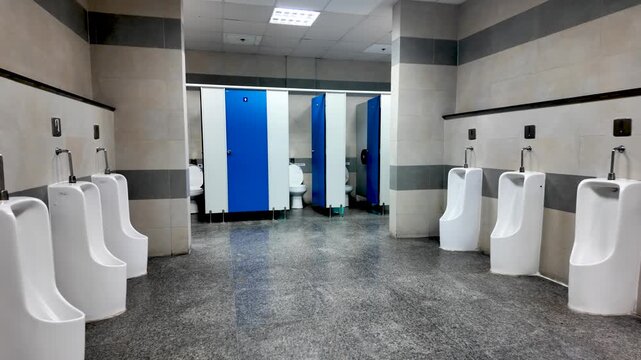 Spacious men's restroom with multiple urinals along tiled walls and blue privacy stalls.