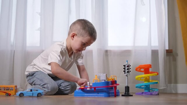 Boy arranges toy ramp carefully. Toddler child leans toward model, interacting. Young learner explores colors. Preschooler fascinated by toy. Student attention on details. Boy is engaged player kid.