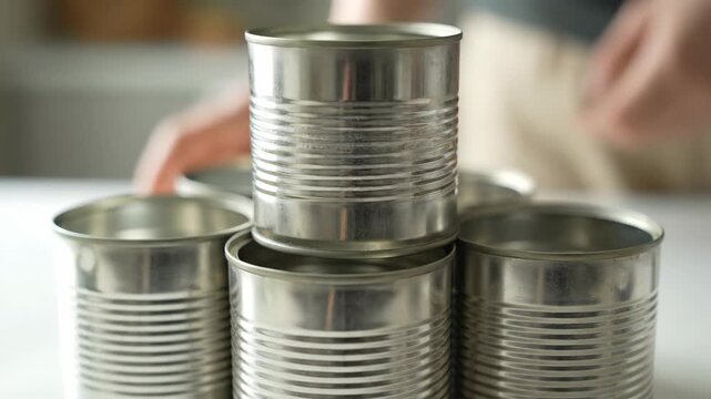 A hand stacks empty tin cans into a pyramid structure. Recycling, reuse, and food storage concept for emergency preparedness
