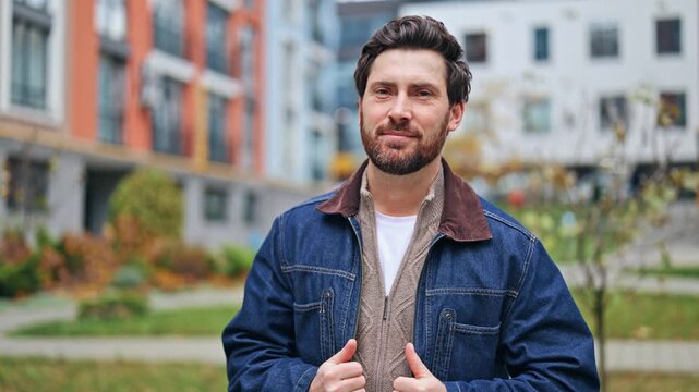 Confident man with a warm smile exudes happiness and positive energy. Standing in a modern urban residential area, conveying a friendly and approachable lifestyle. Joyful, satisfied, and good mood.