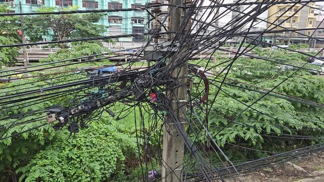 tangled cables, electric poles filled with tangled cables with a tree anf building background. Electric cables or internet lines