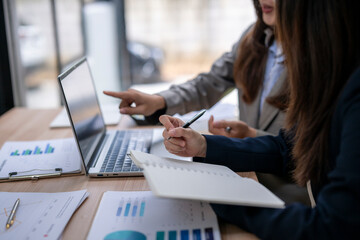 Businesswomen analyzing financial data on laptop and taking notes during office meeting