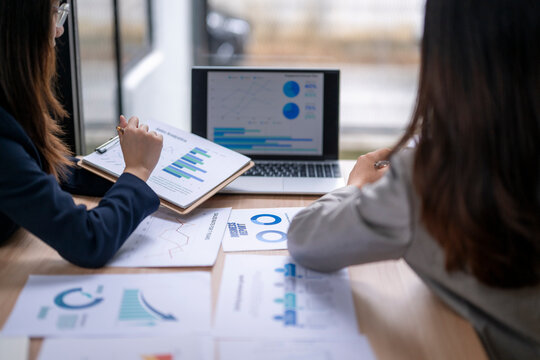 Businesswomen analyzing financial charts and graphs on laptop and documents