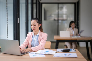 Asian businesswoman working on laptop in modern office analyzing financial charts and graphs