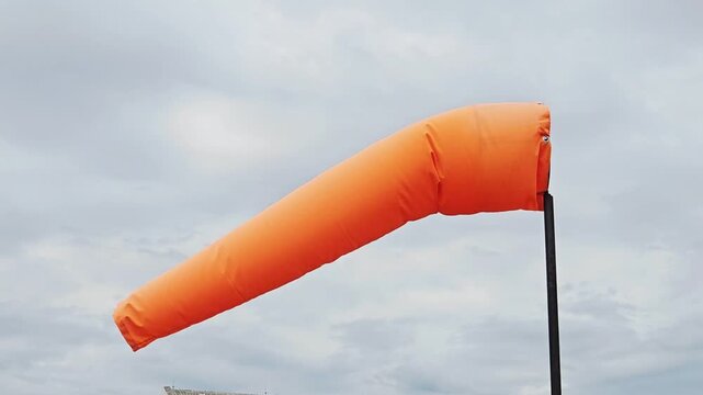  the orange windsock on a pole in strong wind against a blue sky Airbag, wind direction, know which way the wind is blowing on cloundy