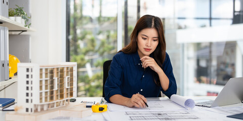 Young asian civil engineer studying a blueprint floor plan and  working with documents, drawings...