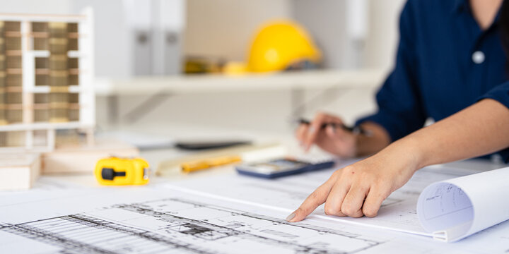 Civil Engineer working on shop drawings of  post tension slab plan on desk with Calculator and triangular scale in construction site office .