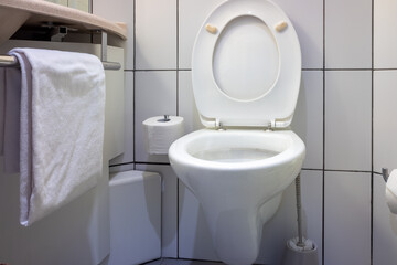 white toilet with its lid up is situated in a bathroom with white tiled walls. roll of toilet paper is mounted to the wall,