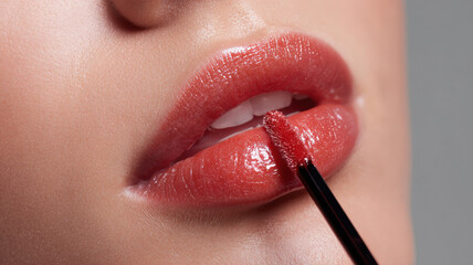 Naklejka premium Applying lip gloss with a close-up focus on the luscious lips and cosmetic applicator