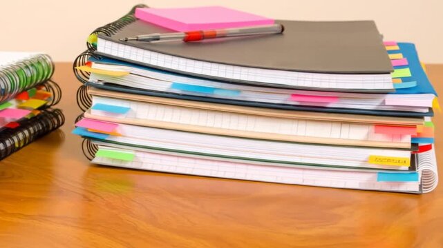 Close-up of stacked spiral notebooks with colorful sticky notes and a pen on a wooden surface
