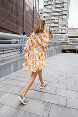 Woman walking away wearing orange dress and sneakers.
