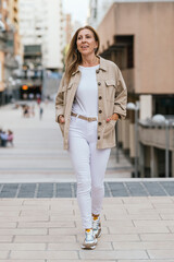 Woman wearing beige jacket and white jeans outdoors.