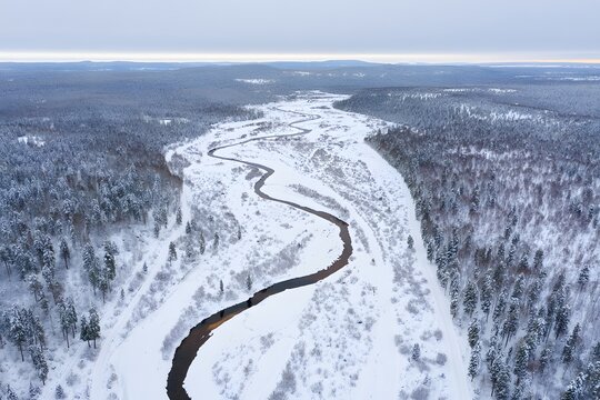Aerial view of a snowy river winding through a forest in winter wonderland scenery