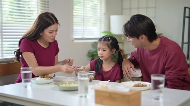 Asian parents encouraging reluctant daughter to eat during family meal