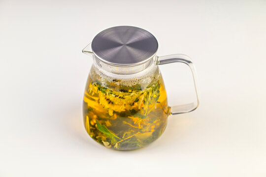 A glass pitcher with a lid and a handle filled with a tea blend