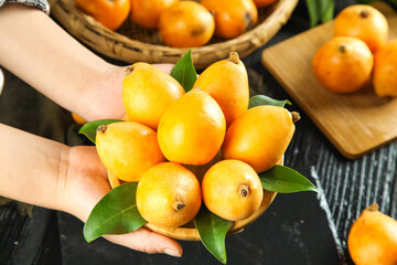 Fresh Loquat Fruits from Yunnan China Held in Hands with Green Leaves and Wooden Basket Background