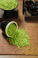Fresh Green Mung Beans Spilling from Bamboo Container with Traditional Tea Service on Wooden Table