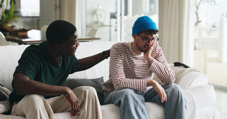 Support, grief and friends on sofa with console, comfort and understanding during bereavement. Mental health, empathy and people in house with conversation, condolences and shoulder rub in mourning.