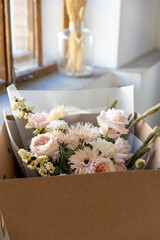 Delicate pastel bouquet with blush pink garden roses, white fringed flowers, and dried accents, carefully packaged in a brown cardboard box for flower delivery.