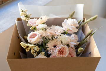 Delicate pastel bouquet with blush pink garden roses, white fringed flowers, and dried accents, carefully packaged in a brown cardboard box for flower delivery.